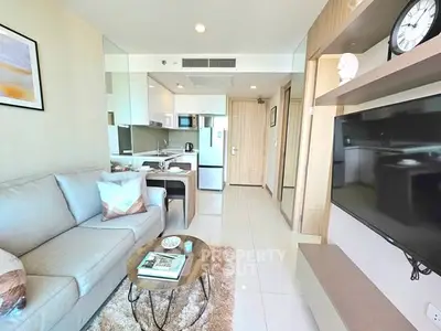Modern living room with open kitchen, sleek furniture, and large TV in a stylish apartment.