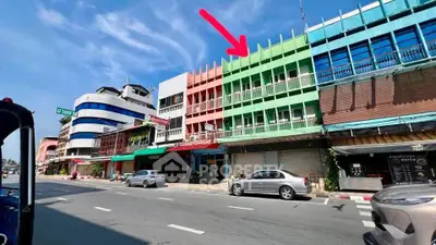 Colorful commercial buildings on a sunny street with parked cars and clear blue sky.