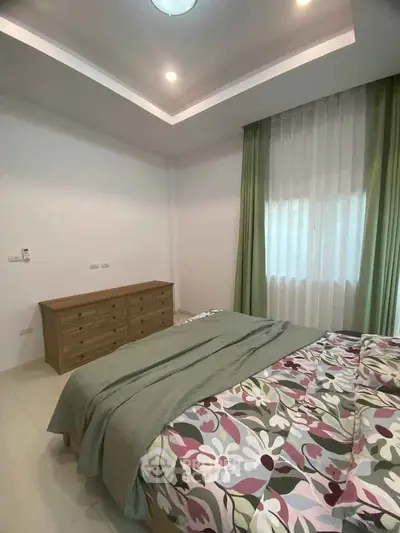 Cozy bedroom with floral bedding and wooden dresser, featuring soft lighting and elegant curtains.
