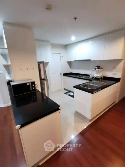 Modern kitchen with sleek black countertops and white cabinetry, featuring a gas stove and stainless steel appliances.