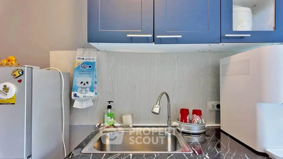 Modern kitchen with sleek cabinetry and marble countertop, featuring a compact fridge and stylish sink area.