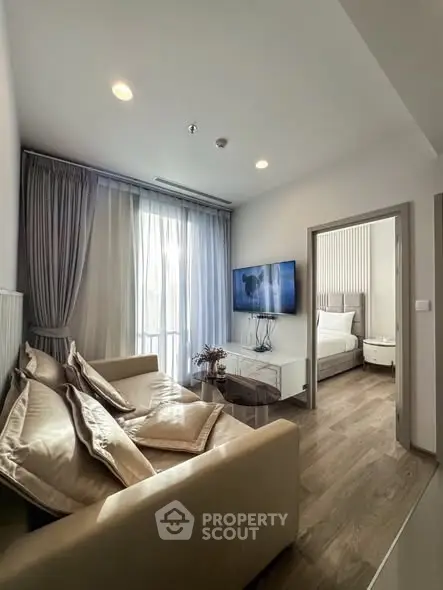 Modern living room with cozy beige sofa and wall-mounted TV, leading to a stylish bedroom.