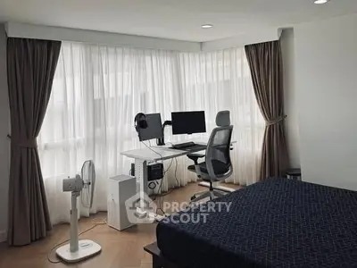 Modern bedroom with study area featuring desk, chair, and dual monitors by large windows.
