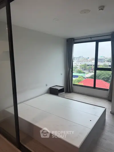 Modern bedroom with large window offering city view, featuring minimalist design and natural light.