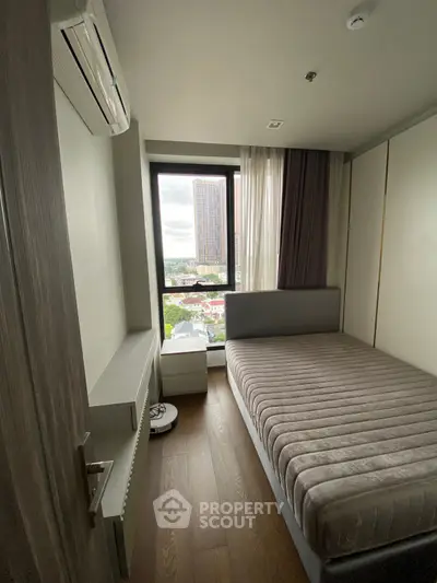 Cozy bedroom with large window offering city view, featuring modern furnishings and air conditioning.