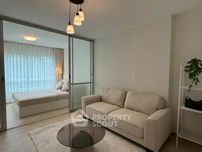 Modern living room with cozy sofa and view into elegant bedroom through glass doors.