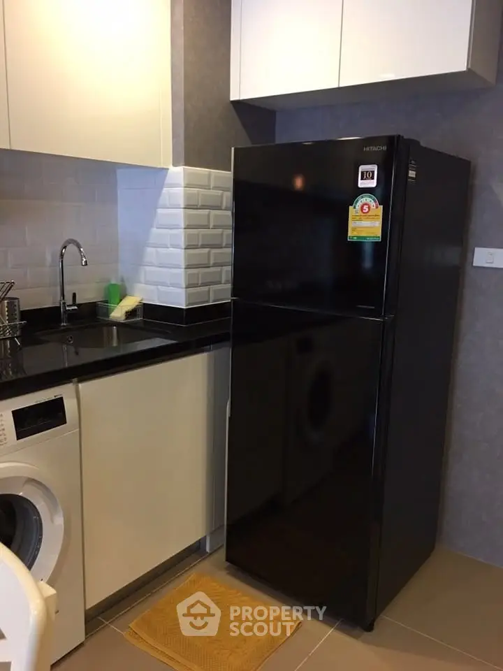Modern kitchen with sleek black fridge and washing machine, featuring stylish backsplash and ample storage.