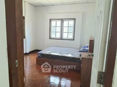 Cozy bedroom with wooden flooring and natural light from large windows.