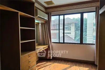Spacious bedroom with large window and built-in wooden shelves in urban apartment
