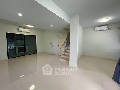 Spacious modern living room with sleek tile flooring and staircase, featuring air conditioning and ample natural light.
