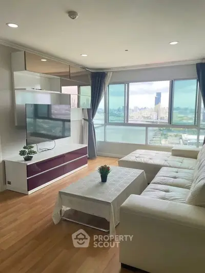 Spacious living room with large windows offering stunning city and river views, modern furniture, and natural light.