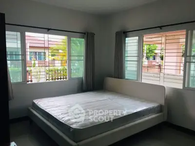 Bright bedroom with large windows and a comfortable bed, offering a serene view.