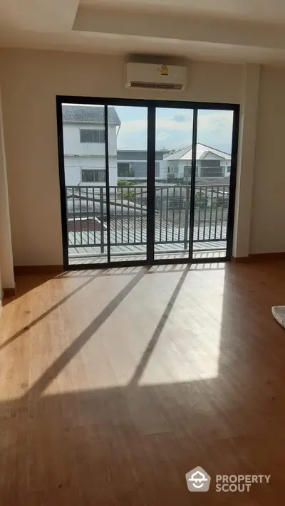 Sunlit spacious living room with large sliding doors opening to a balcony, offering a serene suburban view, perfect for relaxation and entertainment.