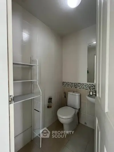 Compact bathroom with modern fixtures and tiled walls, featuring a toilet and shelving unit.