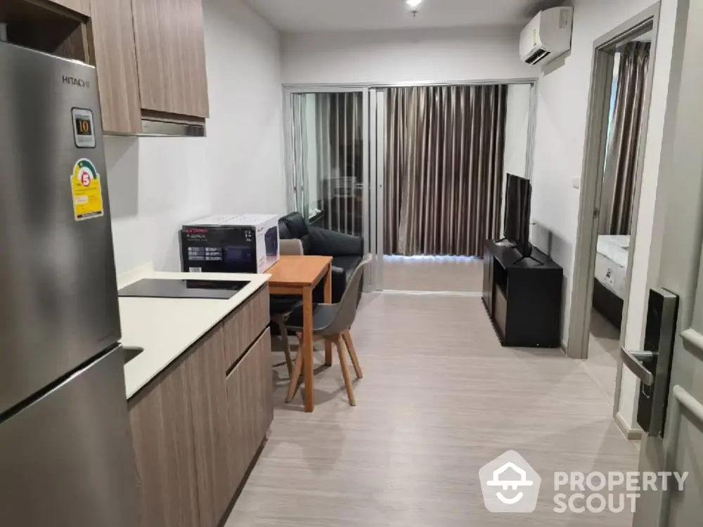 Modern apartment interior with kitchen and living area, featuring sleek wooden cabinetry and contemporary furnishings.