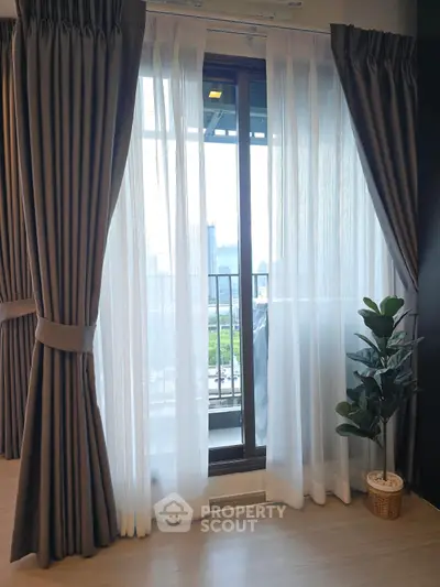 Modern living room with large window and elegant curtains overlooking city view.