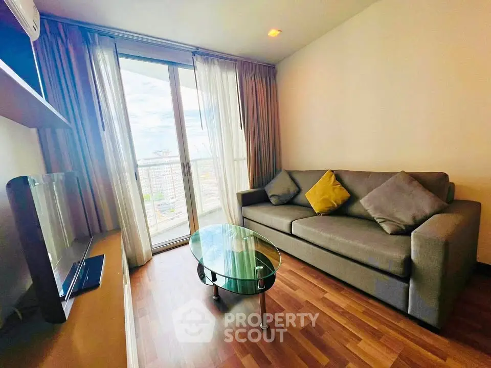 Modern living room with cozy sofa and glass coffee table, featuring large windows with city view.