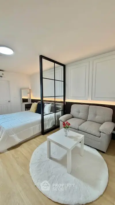 Modern bedroom with cozy sofa and stylish decor, featuring a large mirror and elegant lighting.