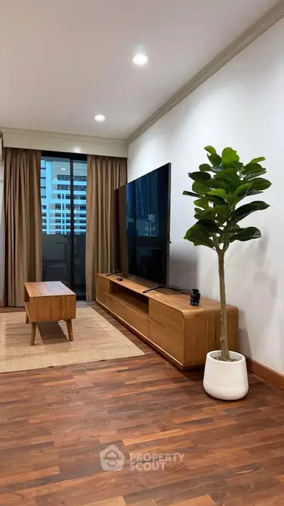 Modern living room with sleek wooden furniture and large TV, featuring a stylish indoor plant and city view.