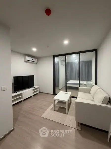 Modern living room with sleek furniture and glass partition to bedroom