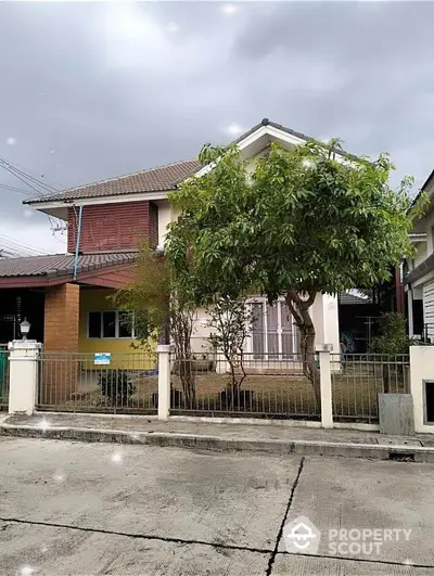 Charming two-story home with a lush front yard tree, offering a cozy suburban retreat under a serene sky, complete with a secure fence and inviting facade.