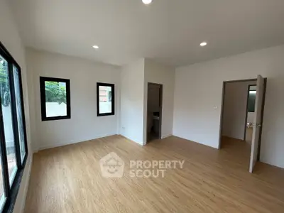 Spacious empty room with wooden flooring and large windows, perfect for customization.