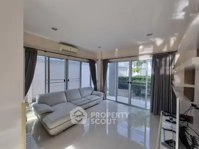 Spacious living room with modern white sofa and large windows offering garden view.