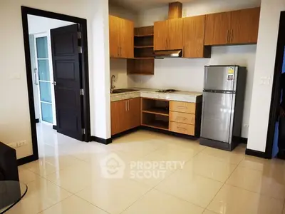 Modern kitchen with wooden cabinets and stainless steel fridge in open layout apartment.