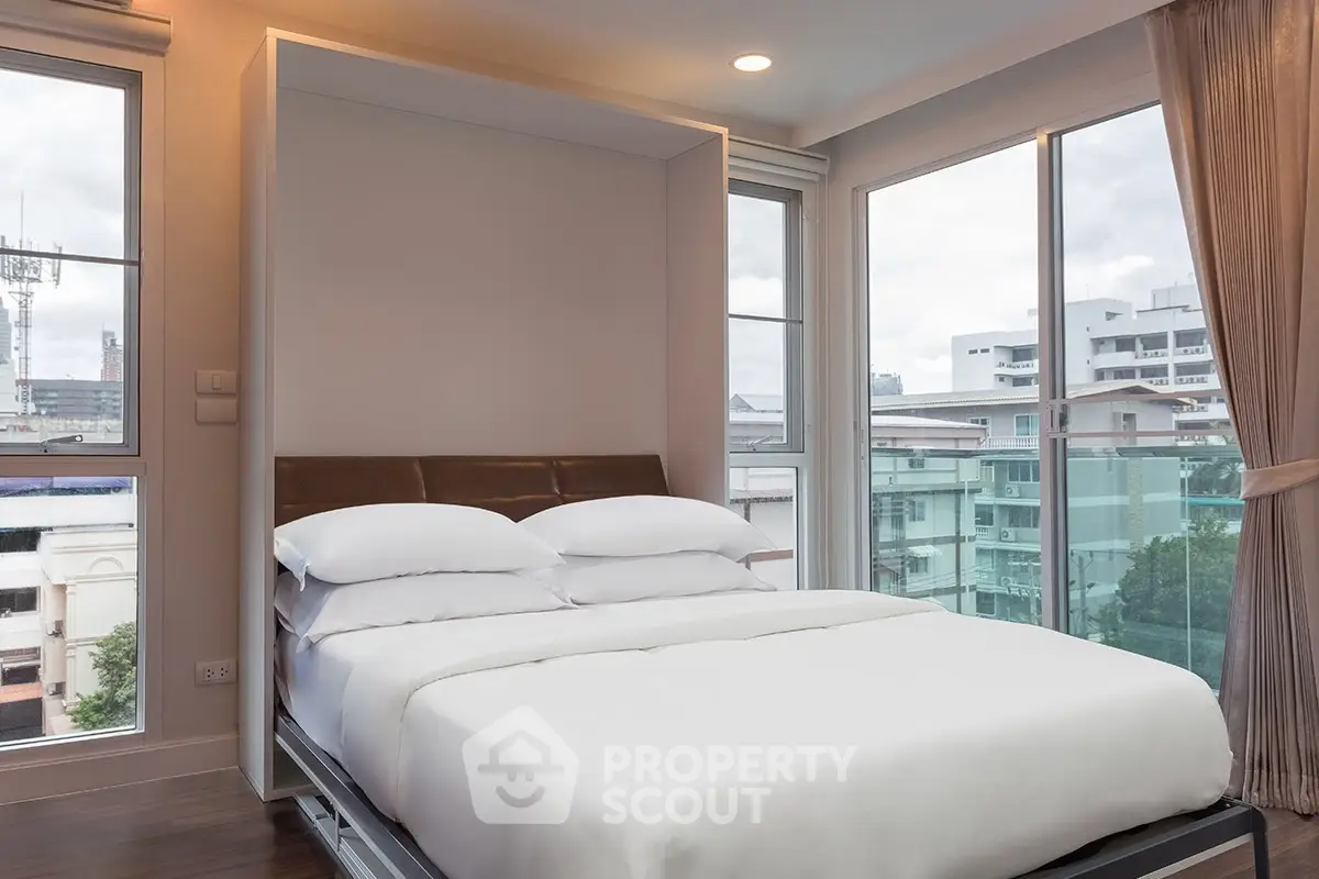 Modern bedroom with large windows and city view, featuring a comfortable bed and elegant decor.