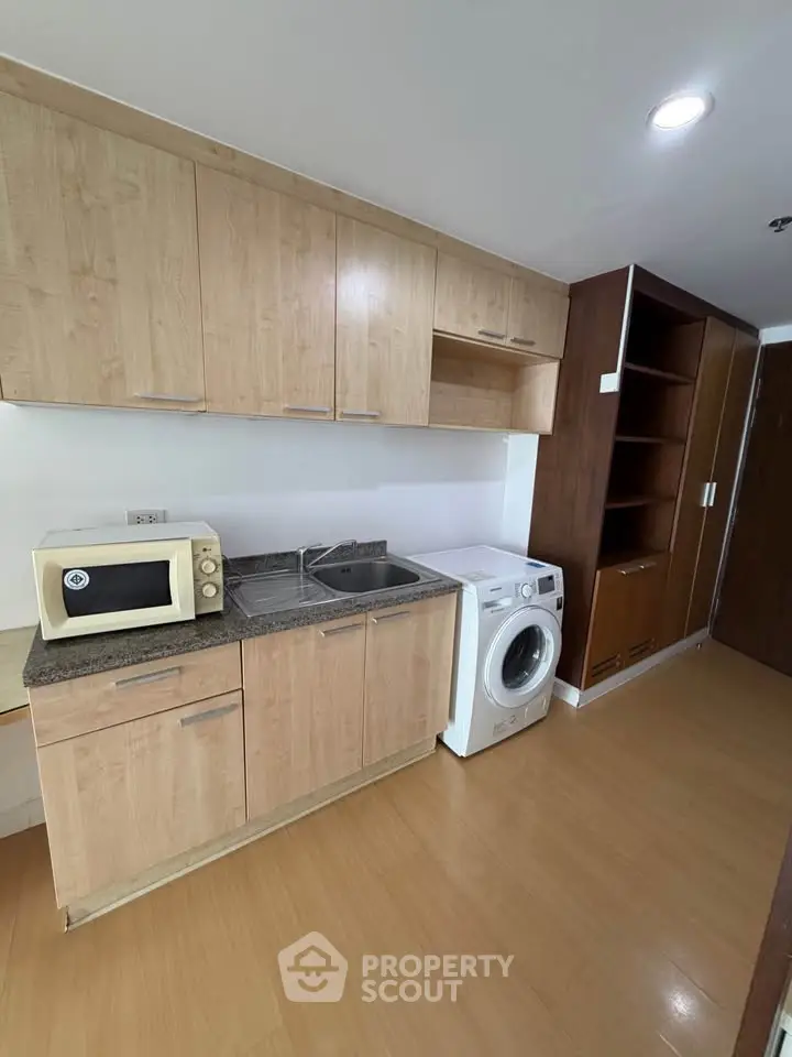 Modern kitchen with wooden cabinets, microwave, and washing machine in a compact layout.