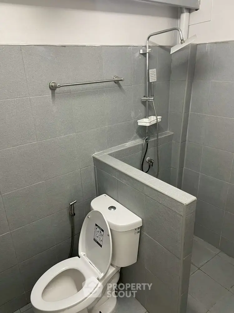 Modern minimalist bathroom with shower and toilet in sleek gray tiles.