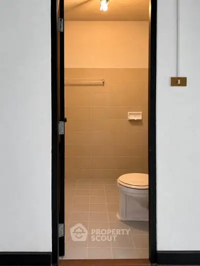 Minimalist bathroom with tiled walls and floor, featuring a toilet and towel rack.