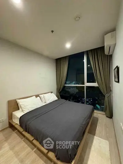 Modern bedroom with city view, featuring a cozy bed and large window with curtains.