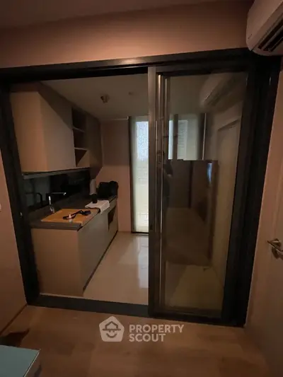 Compact kitchen with sliding glass door and modern appliances in cozy apartment.