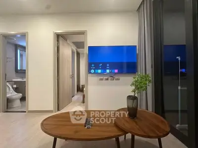 Modern living room with sleek TV and stylish wooden tables, adjacent to a bathroom and hallway.