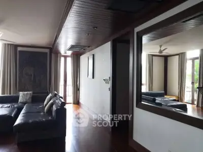 Luxurious living room with elegant wooden flooring and large mirror, featuring a stylish leather sofa and serene decor.
