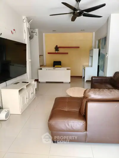 Spacious living room with modern leather sofa and large TV, ideal for relaxation and entertainment.