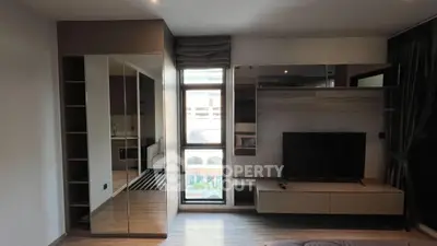 Modern living room with sleek TV unit and mirrored storage, featuring a large window for natural light.