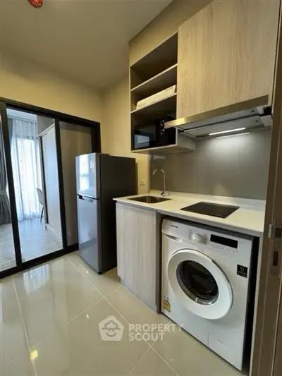 Modern compact kitchen with washing machine and fridge in sleek apartment.