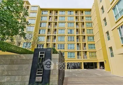 Modern yellow apartment building exterior with lush greenery and spacious entrance.