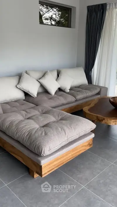 Modern living room with stylish gray sofa and wooden coffee table, featuring large windows and elegant curtains.