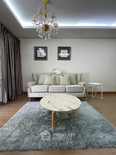 Elegant living room with plush sofa, chandelier, and marble coffee table on a soft rug.