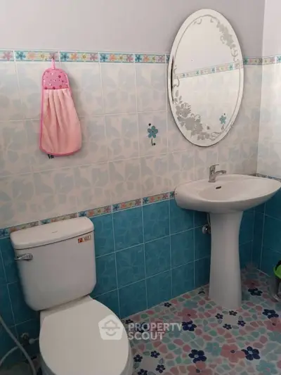 Charming bathroom with floral tiles and oval mirror, featuring a pedestal sink and toilet.