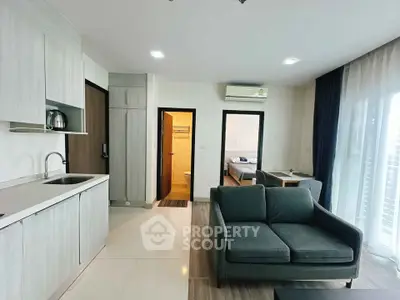 Modern open-plan living room with kitchen and bedroom view, featuring sleek design and natural light.