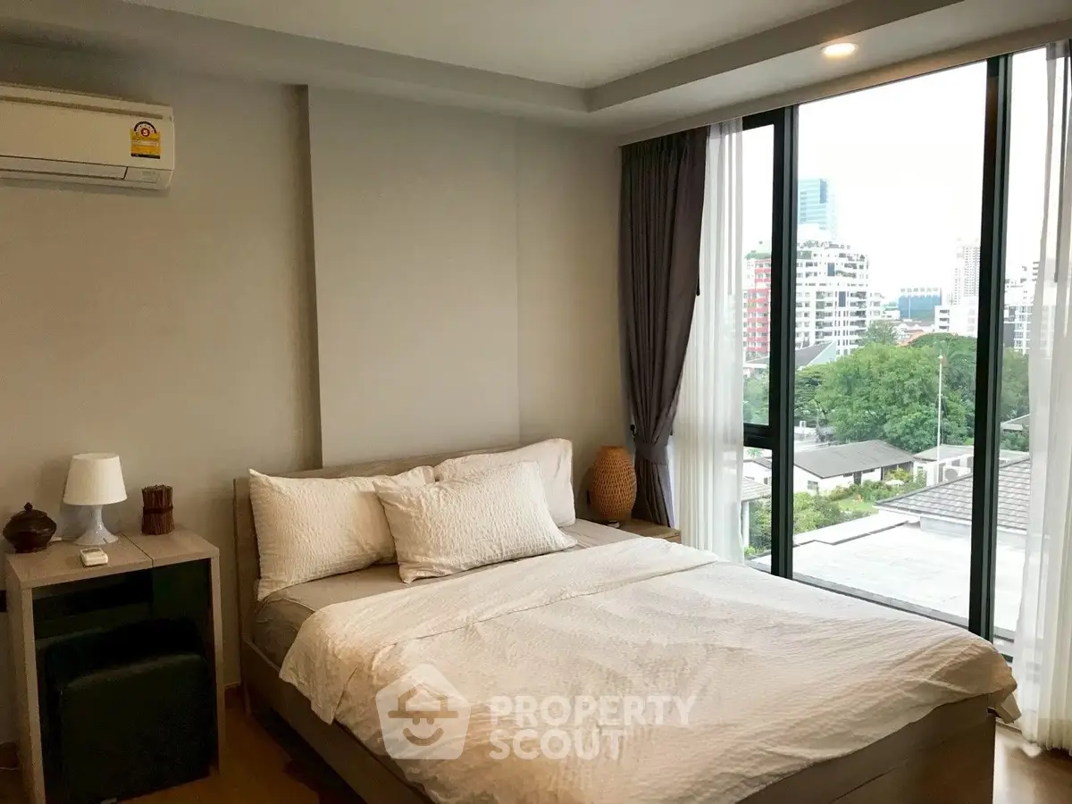 Modern bedroom with large windows offering city views, featuring a cozy bed and stylish decor.