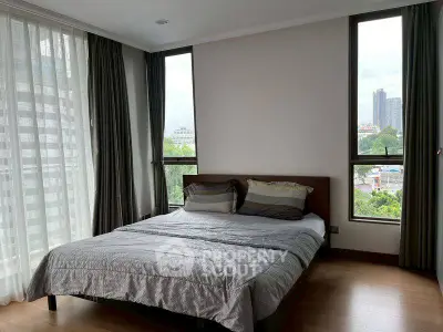 Spacious bedroom with large windows offering city views in modern apartment.
