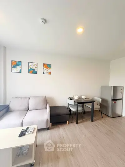 Modern living room with cozy sofa, dining table, and sleek fridge in open layout apartment.