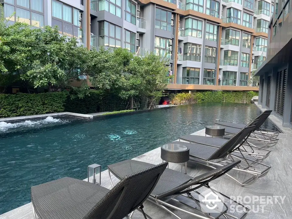 Luxurious condominium pool area with modern lounge chairs and lush greenery