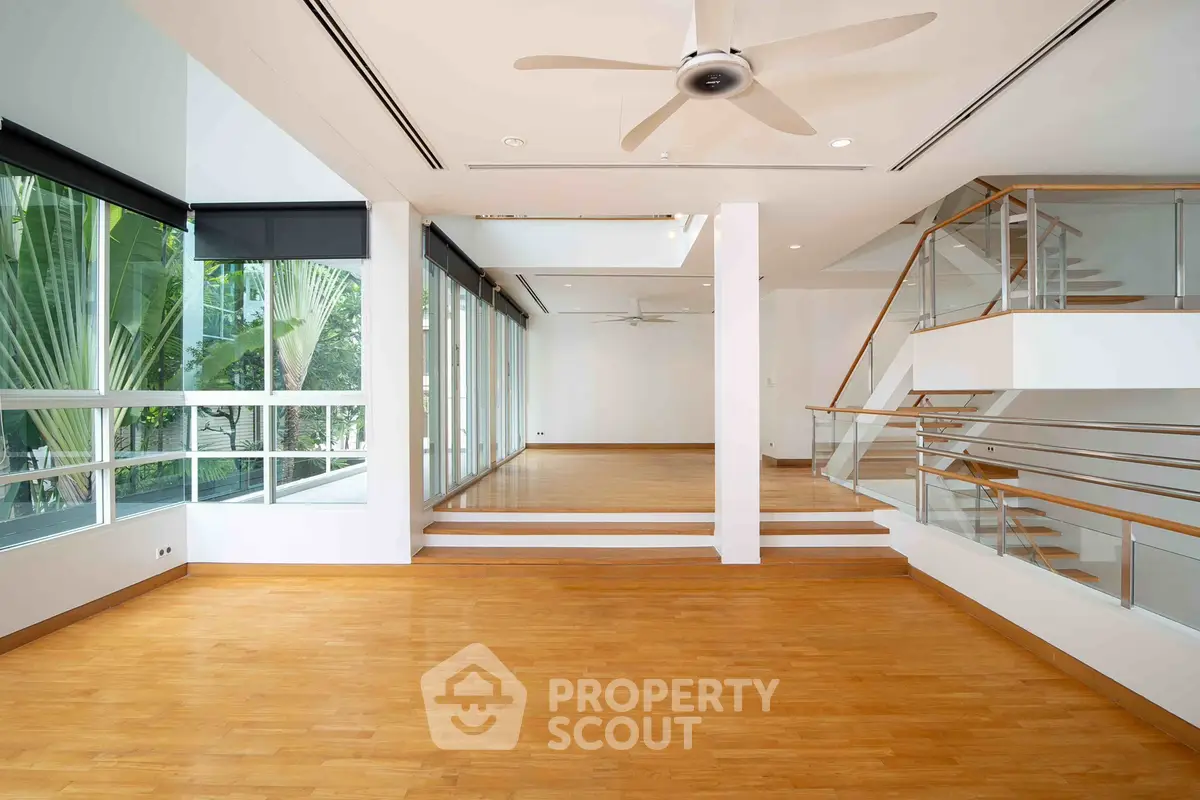 Spacious modern living room with wooden floors and large windows offering lush garden views.