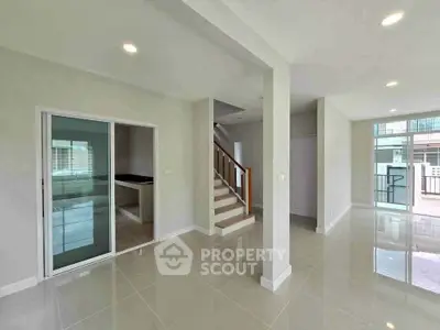 Spacious modern living area with sleek tile flooring and natural light, featuring a staircase and sliding glass doors.